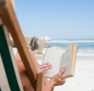 Woman sitting in deck chair at the beach reading