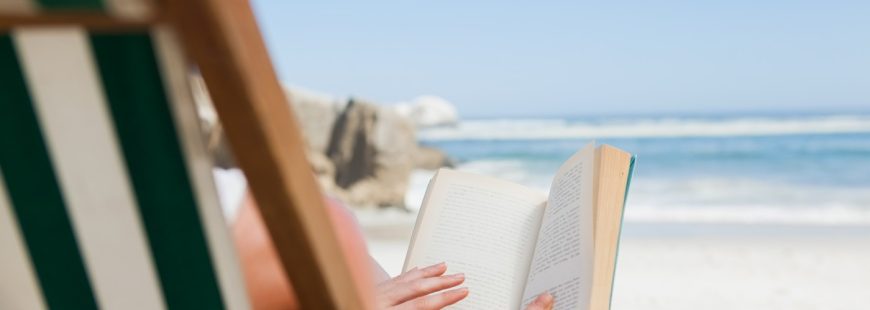 Woman sitting in deck chair at the beach reading