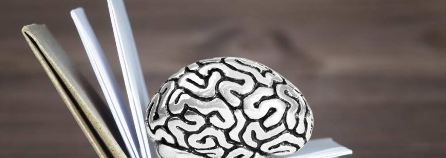 Miniature human brain steel model lying inside an open book against a wooden table background. Mind exercising concept.